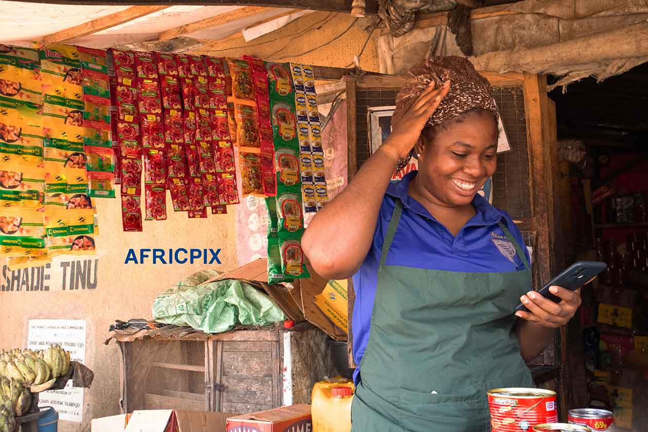 Happy African Market Woman Using Phone with Hand on Head in Joy